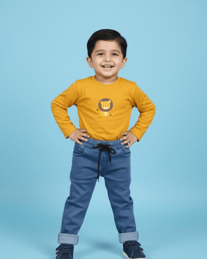 Child wearing a yellow shirt with a lion design and blue jeans on a light blue background