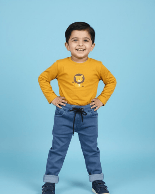 Child wearing a yellow shirt with a lion design and blue jeans on a light blue background