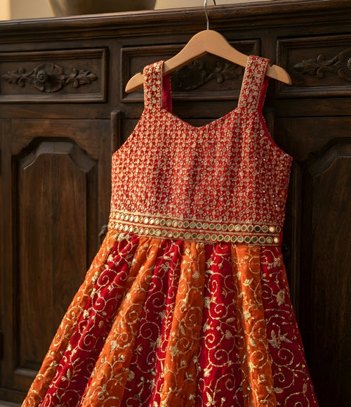 Red and orange patterned dress hanging on a wooden hanger against a dark wooden background